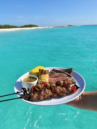 Plato de comida a la parrilla servido a bordo del yate con aguas turquesas del Caribe al fondo