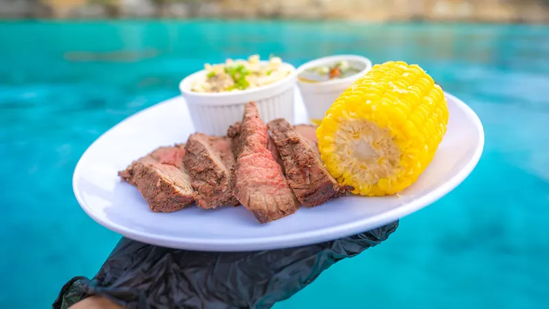 Filete a la parrilla con maíz y guarniciones junto al agua turquesa